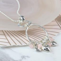 Peace Of Mind. Long silver plated necklace with a double hoop pendant featuring a cluster of silver plated rings, pink c